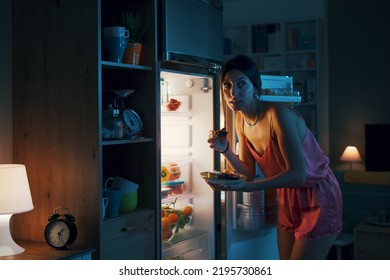 Hungry Woman Looking In The Fridge And Eating Delicious Pastries At Night, She Is Breaking Her Diet