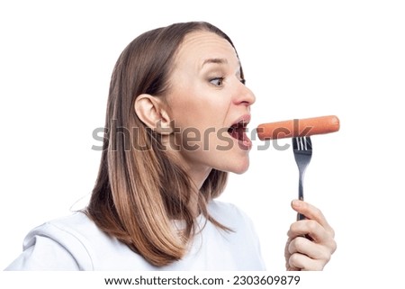 A hungry woman with an open mouth eats a sausage from a fork. Delicious fast junk food. Isolated on a white background. Close-up.