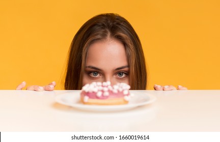 Hungry Woman Peeking Out Of Table Starving To Eat Donut, Yellow Background With Copy Space