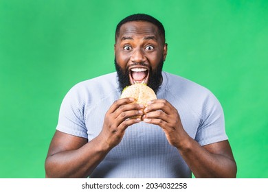 Hungry young african american black man eating hamburger isolated over green background. Diet concept.