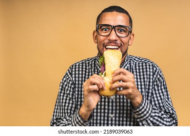 Hungry Young African American Black Man Eating Sandwich Isolated Over Beige Background. Diet Or Fast Food Concept.