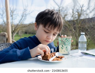 Hungry young boy eating flapjack for dessert,Kid having organic vegan homemade oatmeal bars with cranberries and seeds,Child having snack and relaxing in the garden on sunny day spring or Summer