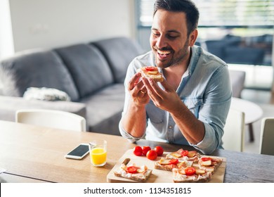 Hungry young man eating sandwich at home