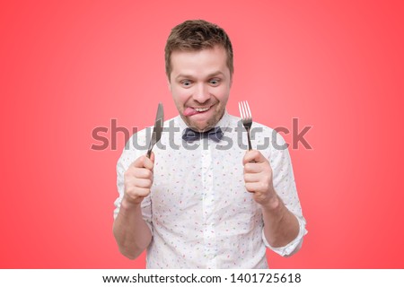 Hungry young man holding fork and knife on hand ready to eat, licking lips. Diet and healthy food concept.
