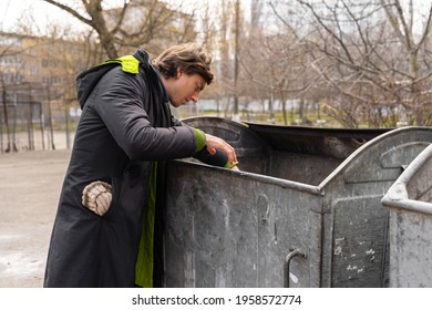 Hungry Young Man Looking For Food In Trash Containers On The Street. Poverty Among Homeless People Forced To Live On The Street. Lifestyle Of Tramp, Living In The Streets.
