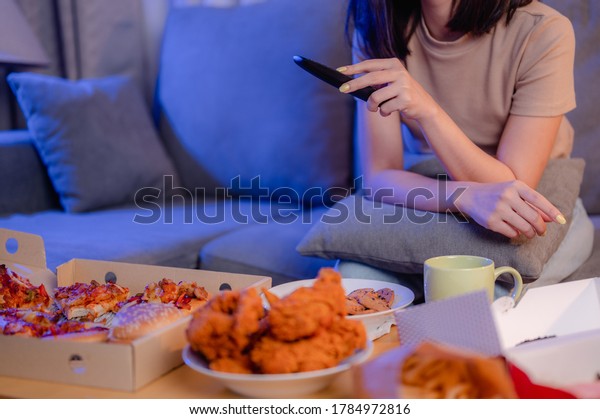 Hungry young woman\
eating junk food Fried Chicken and French Fries for dinner by\
ordering delivery while watching TV, relaxing at home on holiday.\
unhealthy meal, obesity\
risk.
