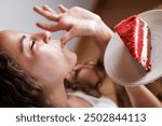 Hungry young woman eating a red velvet cake. Enjoying her celebration. Sugar rush. Sugar cravings. Fun moments eating cake, scooping the cream with fingers. Finger-licking good.