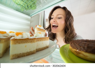 Hungry Young Woman Eating Slice Of Cake From Fridge At Home