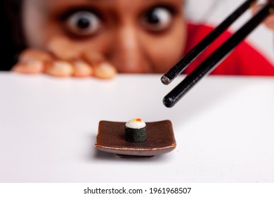 Hungry Young Woman Eyeing A Sushi Starter With Wide Eyes In A Fun Food And Catering Concept Using Miniature Toy Food On A Plate And Chopsticks With Selective Focus