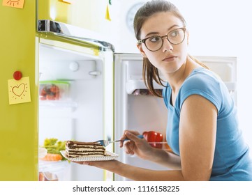 Hungry Young Woman Taking A Delicious Dessert From The Fridge And Having A Snack, Diet Fail Concept