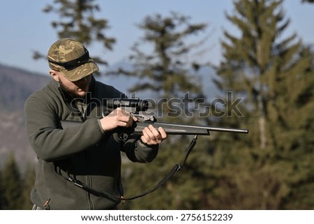 Hunter adjusting rifle scope while preparing for hunting in forested mountain landscape