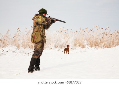 Hunter Aiming At The Prey, Dog Waiting For The Shotgun To Fire. Hunting Winter Open Season Scene