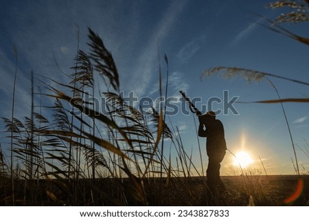 Hunter aiming with rifle while standing against sky