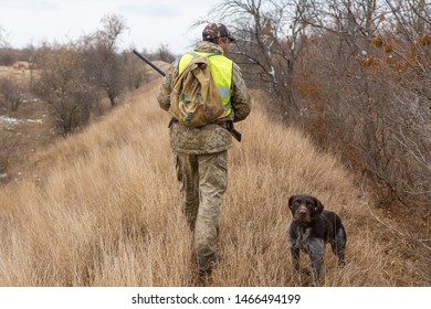 Hunter With A Gun And A Dog Go On The Cold Fall In The Steppe, Hunting Pheasant In A Reflective Vest