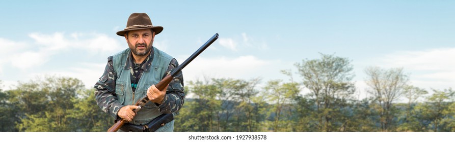 A hunter with a gun in his hands in hunting clothes in the autumn forest in search of a trophy. A man stands with weapons and hunting dogs tracking down the game.