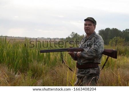 
Hunter with a gun. Portrait of a hunter. Vigilant hunter stands in full growth with a gun in the dry grass. Hunting.
