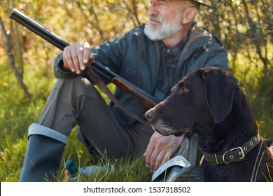 Hunter male in hat, with shotgun, in casual hunting clothes looking away, dog next to him