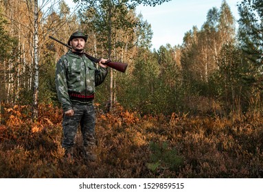 Hunter Man In Camouflage With A Gun During The Hunt In Search Of Wild Birds Or Game On The Background Of The Autumn Forest. Autumn Hunting Season. The Concept Of A Hobby, Killing. Copy Space.