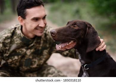 Hunter Man With A Hunting Dog In The Forest. A Man Smiles While Sitting And Stroking His Dog On A Hunt In The Forest. 