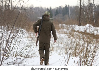 Hunter man with old 16 caliber side-by-side double-barreled shotgun dressed in dark khaki clothing in the forest