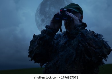 Hunter Observes His Hunting Area With A Night Vision Device Under A Full Moon.
