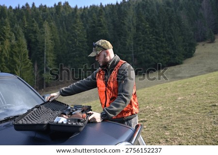 Hunter preparing firearm in hard case on car hood before hunting trip in forest field