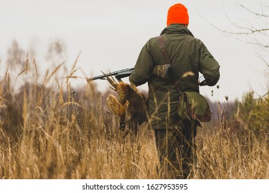 Hunter With Prey, A Pheasant In His Hand At A Field.