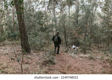 Hunter Walking Downhill In Forest With His Dog