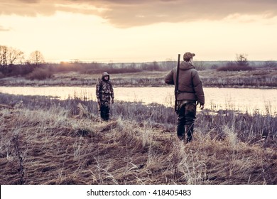 Hunters Choosing A Good Position For Duck Hunting In The Field Nearby River During Sunrise. 