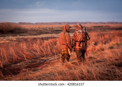 Hunters Looking Out For Prey During Hunting In Rural Field During Sunrise. Field Painted With Orange Color Of Rising Sun