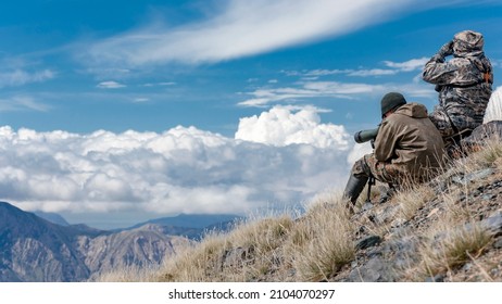 Hunters in the mountains are searching for cautious animals with binoculars and telescope. Hunters in the high mountains are searching for animals using optical devices. 