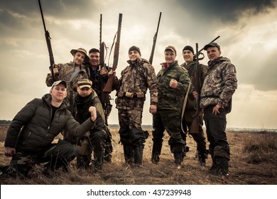 Hunters standing together against sunrise sky in rural field during hunting season. Concept for teamwork.