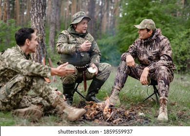Hunters tell how they hunted in the forest while sitting on a halt with friends. Hunters bask near a campfire in a halt in a wild forest. 