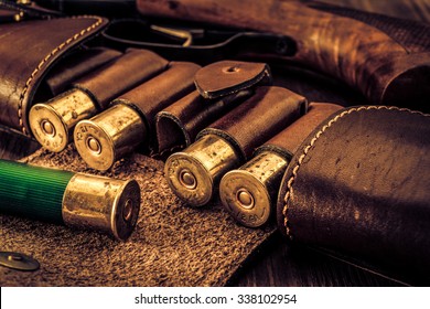 Hunting ammunition 12 gauge in leather bandolier and shotgun on a wooden table. Focus on the cartridges, image vignetting and the yellow-blue toning