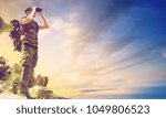 hunting, army, military service and people concept - young soldier with backpack looking to binocular over sky observing area