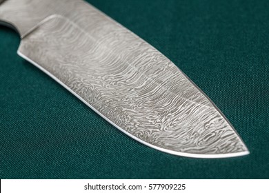 Hunting damascus steel knife handmade on a green fabric, closeup.