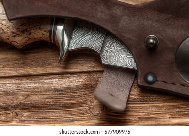 Hunting damascus steel knife handmade in sheath on a brown wooden background, closeup.