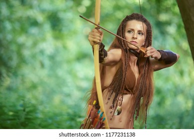 Hunting girl Amazon shoots from a wooden bow in the forest