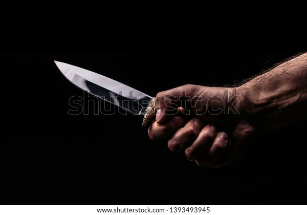 Hunting knife in hand on\
dark background