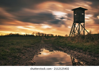 Hunting tower, raised hide in the sunset with moving clouds and reflections an a puddle of water