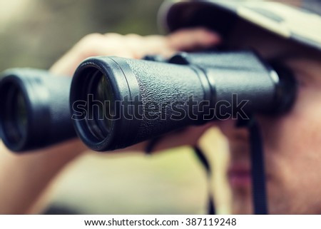 hunting, war, army and people concept - close up of young soldier, ranger or hunter with binocular observing forest