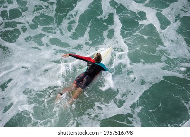 HUNTINGTON BEACH, CA - APRIL 16, 2021: Person Riding Surfboard Out To Waves In Pacific Ocean Off Of Huntington Beach Coast