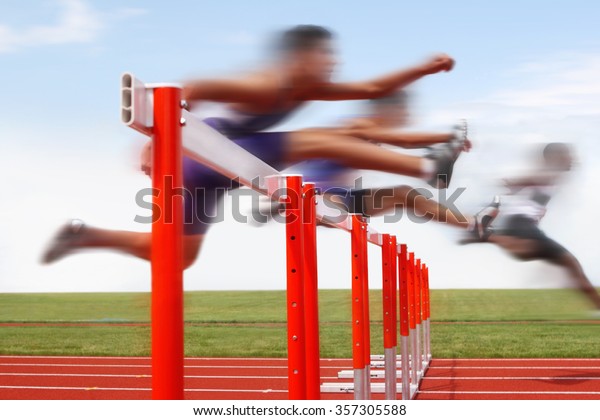Hurdle race, men jumping over hurdles in a track\
and field race. Motion blurred image, digitally altered\
unidentifiable face.