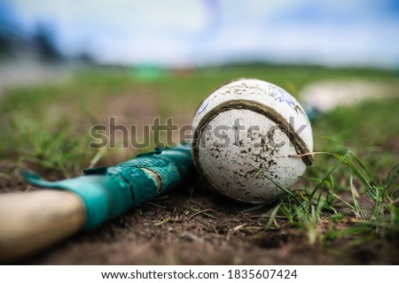 A hurley and a sliothar lie in the grass with a out of focus background