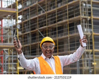 Hurrah, Exulting And Joyful Indian Engineer Holding Rolled Up Plans On Construction Site