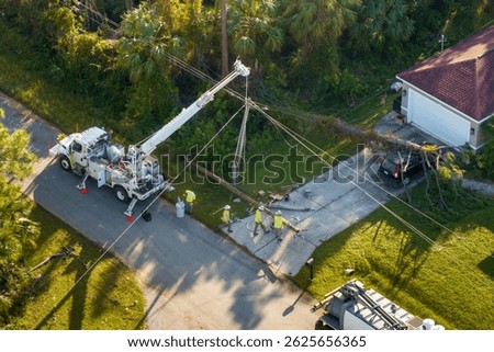 Hurricane aftermath in Florida. Workers using bucket trucks to repair blown down electrical wires at residential house. Utility services fixing damaged power lines