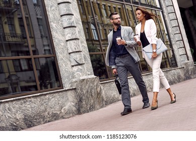 Hurry For Meeting. Two Young Business People Walking Outside On The City Street Drinking Hot Coffee Talking Smiling Joyful