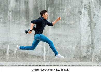 Hurrying to be first. Full length of young photographer running against a concrete wall - Powered by Shutterstock