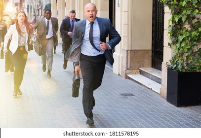 Hurrying Business People With Stressed Man In Foreground Running On City Street.