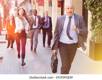 Hurrying Business People With Stressed Man In Foreground Running On City Street.